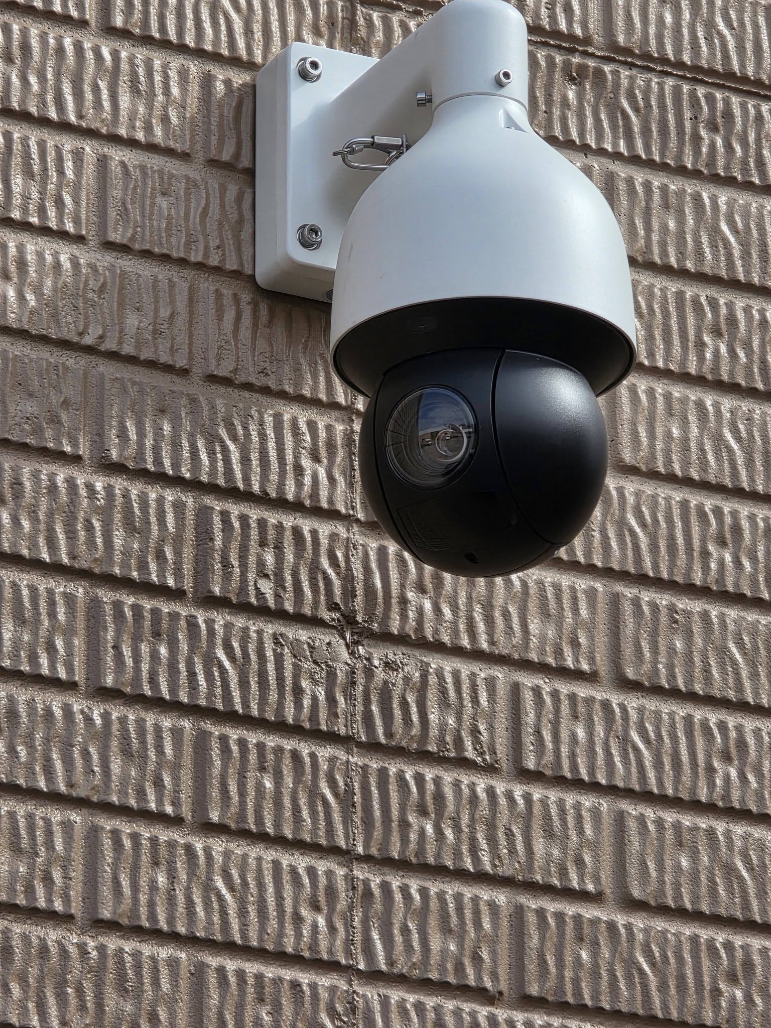 PTZ dome security camera mounted on commercial warehouse exterior brick wall